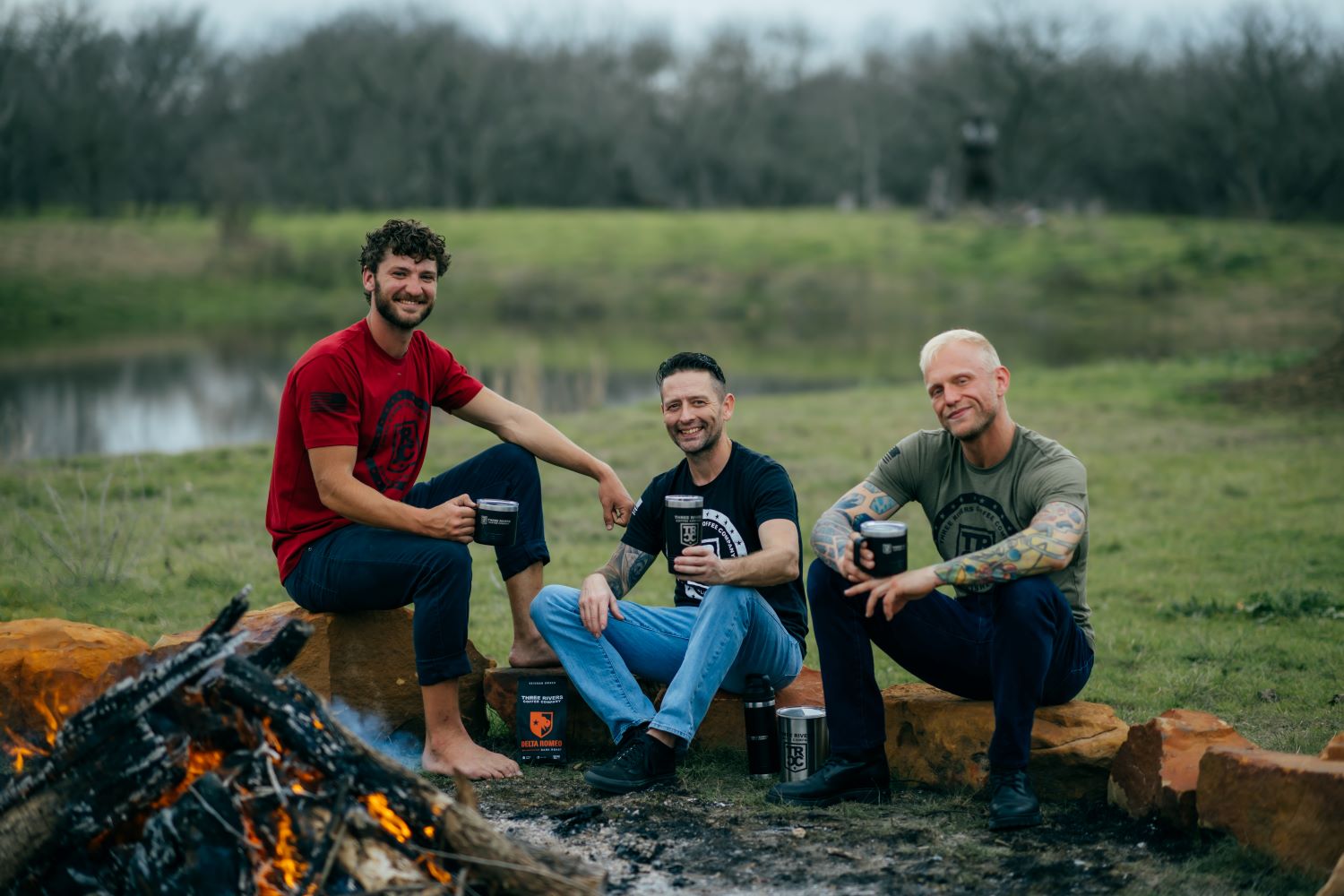 3 men wearing TRCC 22 stars tshirt sitting by fire 